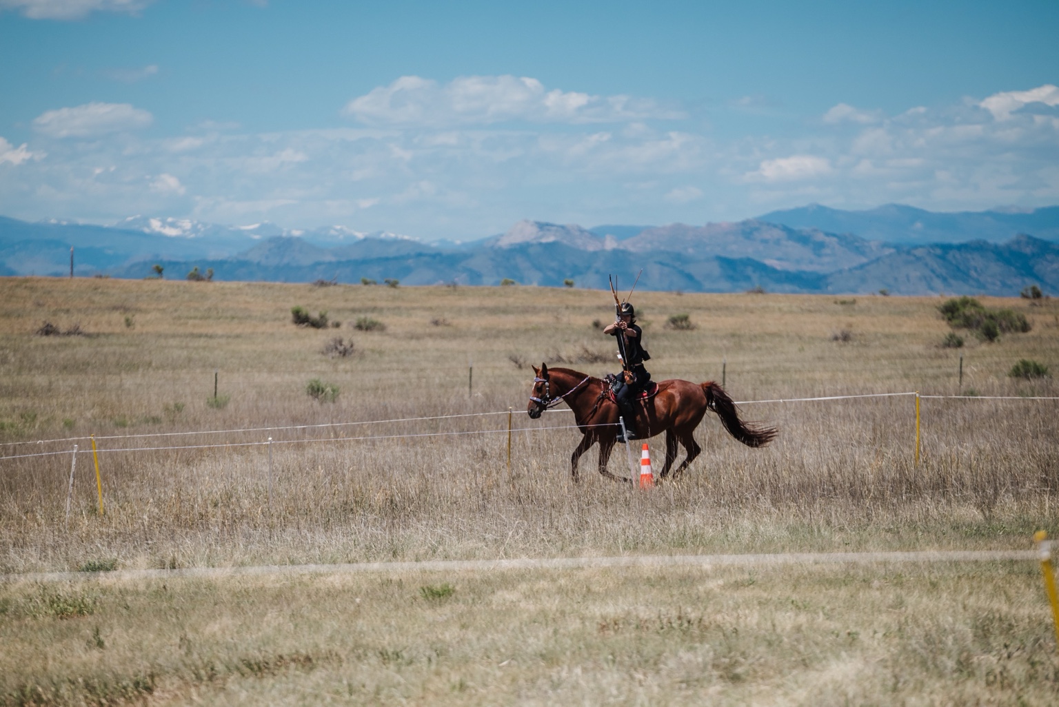A mounted archer competing on a grass course with mountains in the background