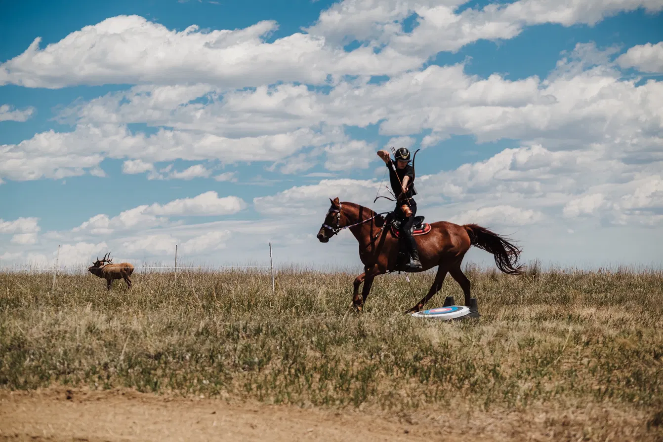 The author riding a brown horse with a traditional bow in an open field