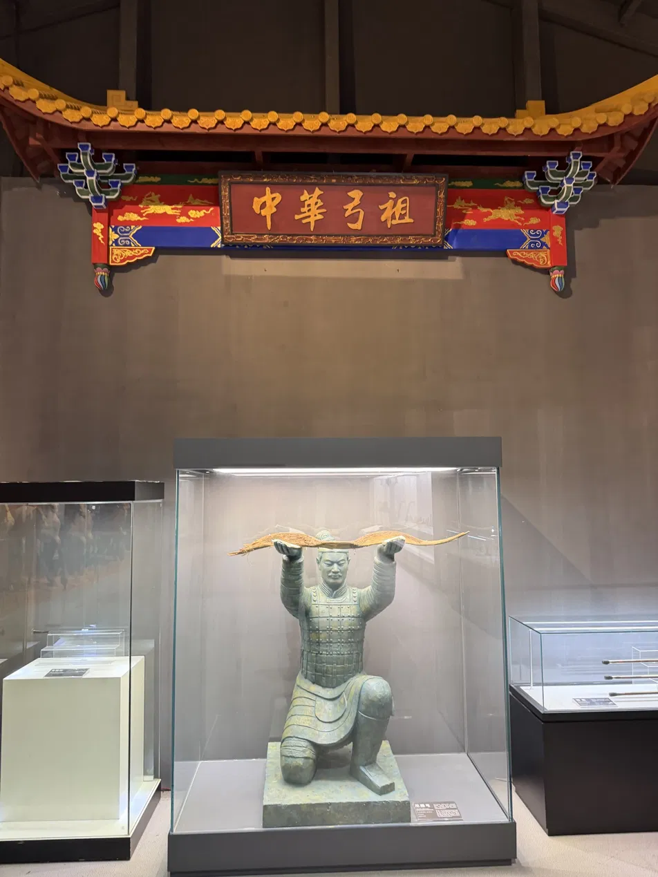 A kneeling exhibition figure holding a bow beneath a decorated sign
